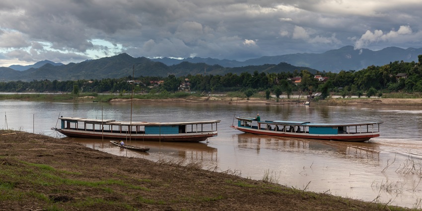Boats located on the river with dark clouds, lush greenery and distant mountains
