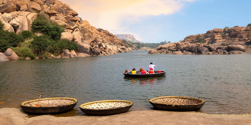 Tourists enjoy a coracle boat ride on the Tungabhadra river valley at sunset in Hampi