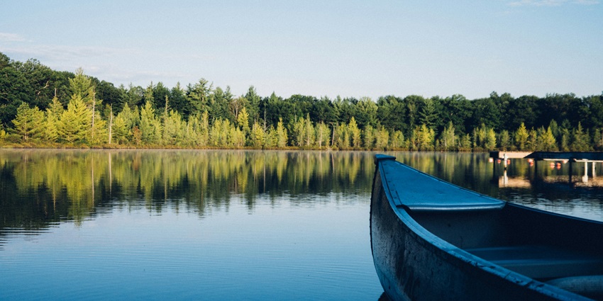 A serene lake with emerald-green water surrounded by lush greenery and rocky mountains.
