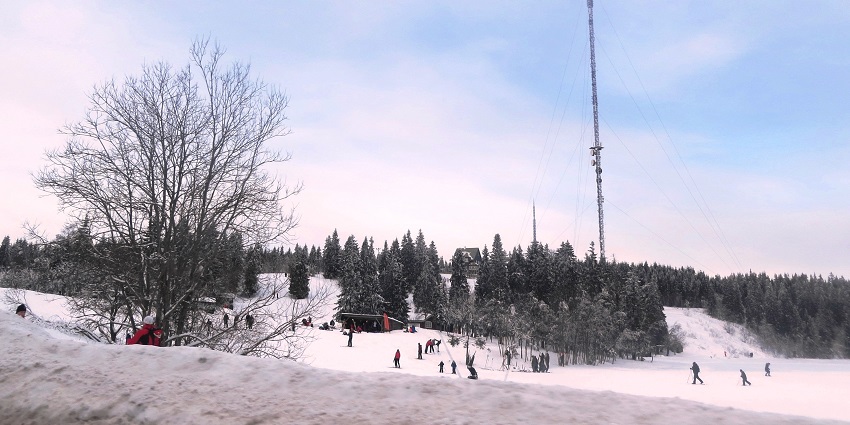 An Image of the Tryvann showcasing a snowy landscape in Oslo with people skiing in the background.