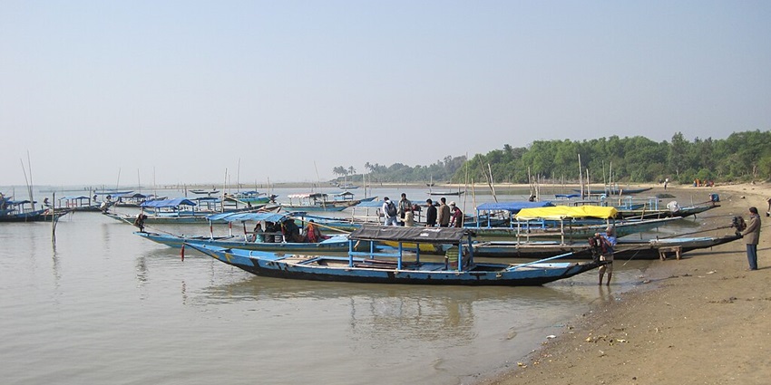 Multiple blue-coloured boats parked at the shore of Chilika Lake and people standing by
