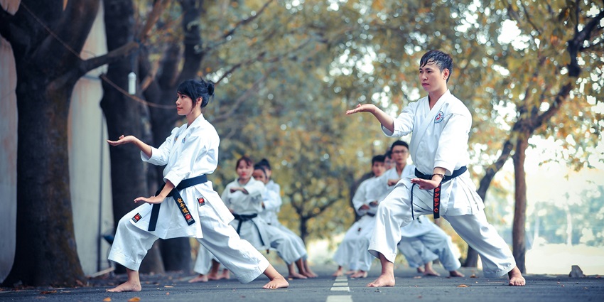 Two people practicing karate on an empty road under a clear sky with mountains in the background
