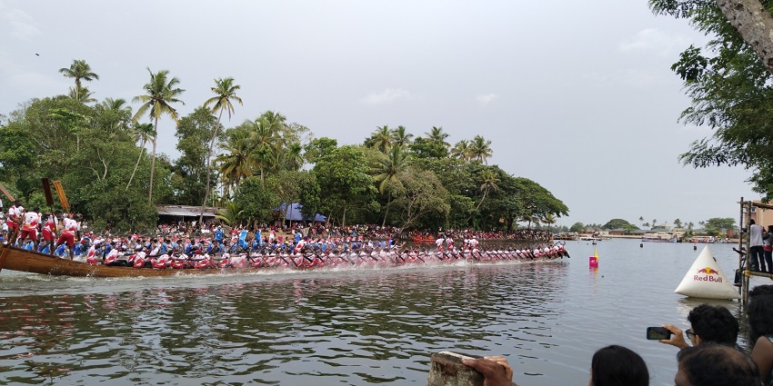 People sitting on a long boat taking part in the Nehru trophy race with people watching them.