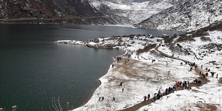 Changu lake in Sikkim, with snow-covered mountains and people walking along the snowy edge