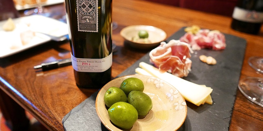 Bottle of Inglenook extra-virgin olive oil alongside fresh green olives and tasting plates