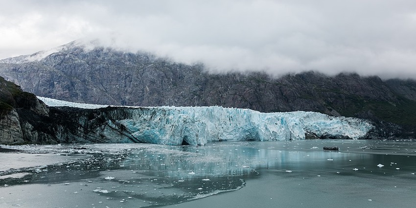 Majestic glacier calving into the ocean, with a mountain backdrop obscured by clouds.