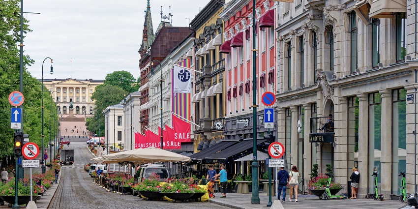 An image of Karl Johans gate in Oslo, showing colourful buildings, shops, and the Royal Palace.