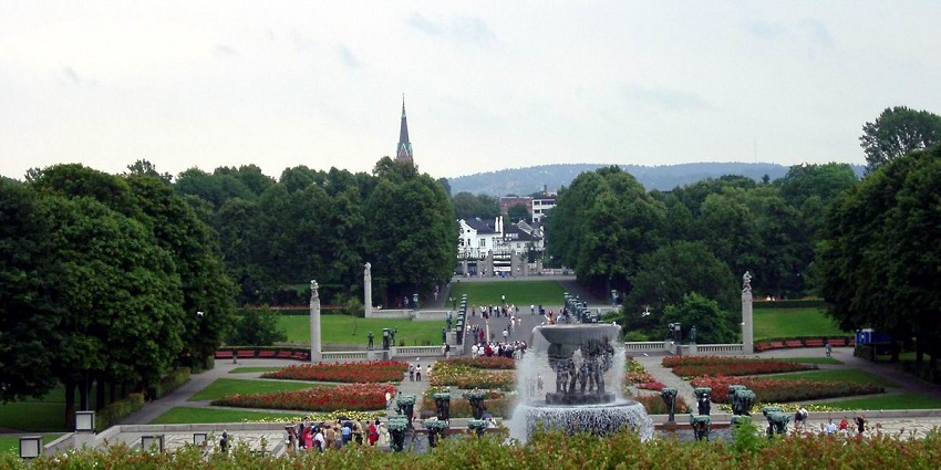 An image of a serene park in Oslo with a fountain, pathways and a church spine visible in the background.