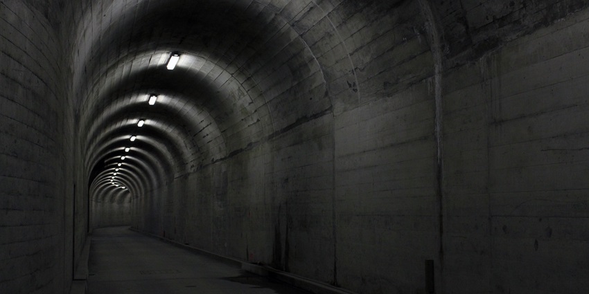 Dark tunnel with concrete walls and dim overhead lighting resembling Underground Vaults