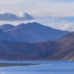 Pangong tso with a bird flying, clear water, small rocks in the lake and distant mountains