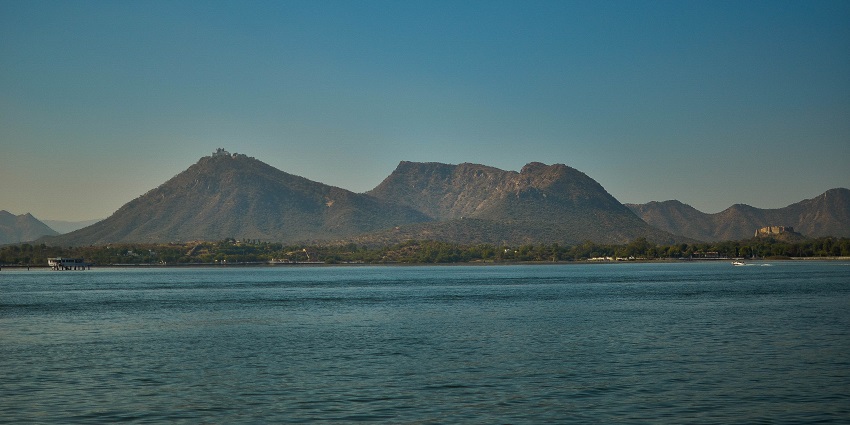 Fateh Sagar Lake with a motorboat rowing in the waterbody and distant green mountains.