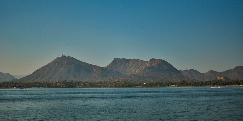 A peaceful morning scene at Lake Fatehsagar, with a speed boat on the water and hills.