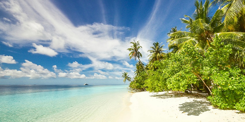 A tropical beach with white sand, turquoise water, palm trees, and a cloudy blue sky