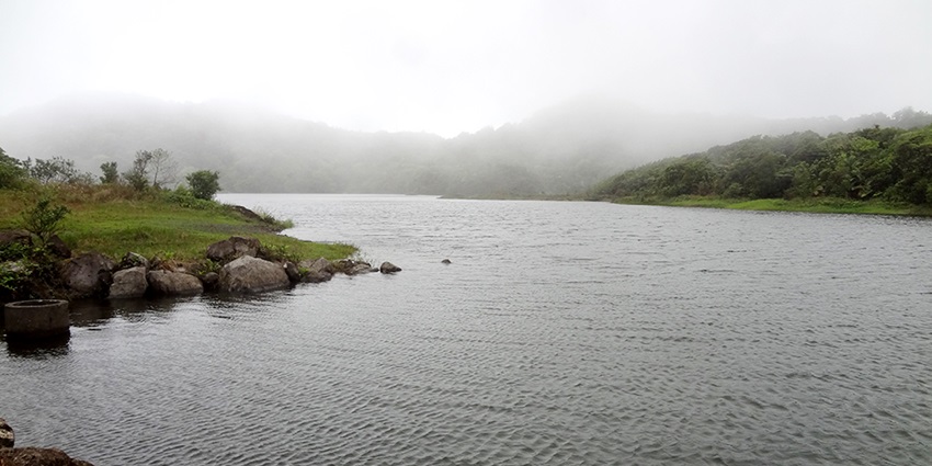 View of Freshwater Lake surrounded by small rocks, green bushes, one of the pretty lakes in Dominica.
