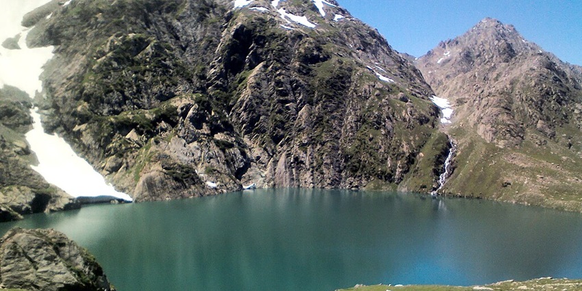 Gadsar Lake with a bright blue water body, surrounded by mountains covered with snow