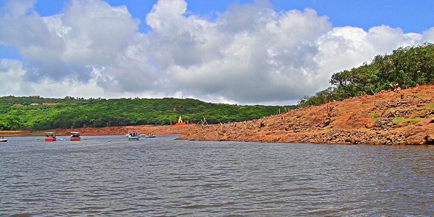 Lake with sandy shorelines, multiple boats in the lake, a distant temple and green hills