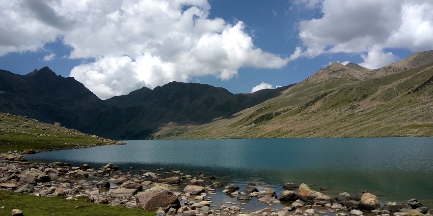 Gangabal Lake with rocks on the shore and surrounded by mountains under the cloudy sky