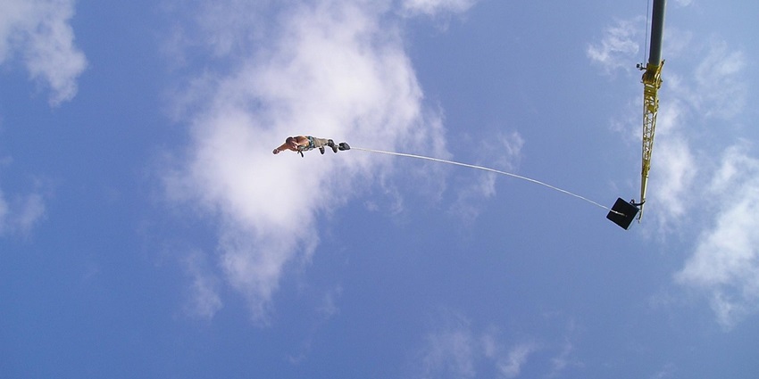 An Image of a man bungee jumping from a platform, harnessed to a yellow rope in Goa