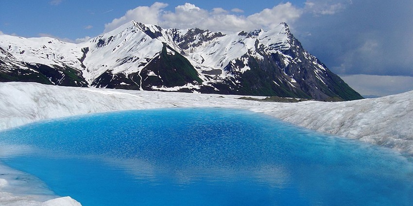 Small lake with very bright blue water surrounded by ice and snow-covered mountains.