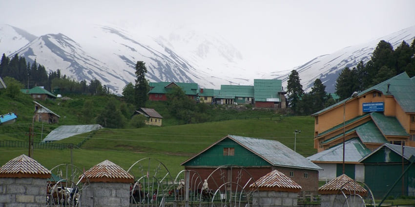 Gulmarg near Dal Lake in January with small houses, tall trees, and snowy mountains