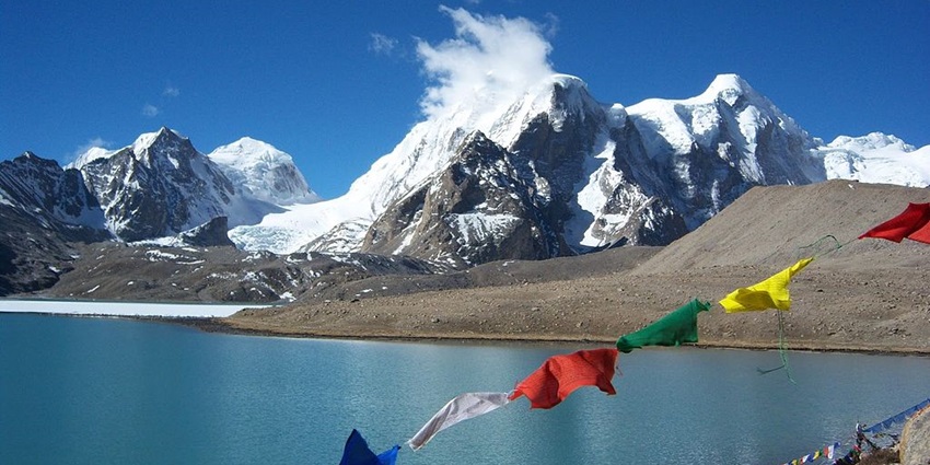 Gurudongmar Lake with multiple Buddhist flags fluttering and mountains covered in snow.