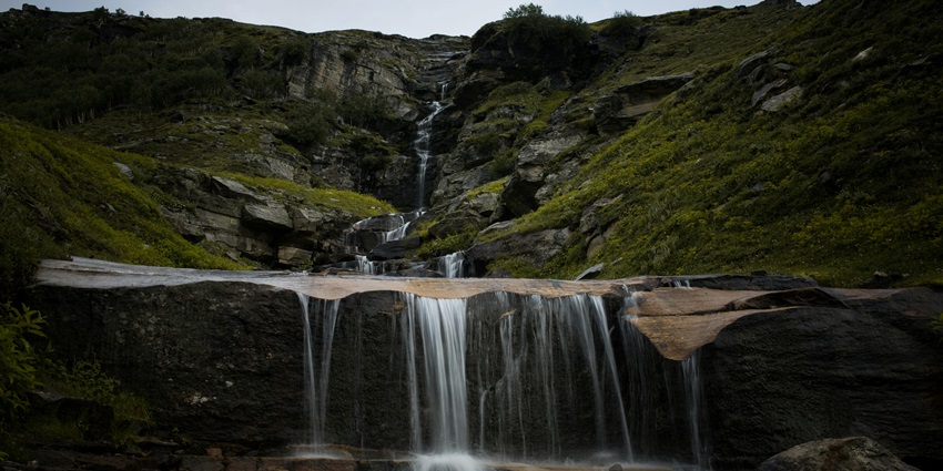Scenic waterfall cascading through rocks surrounded by lush greenery in Himachal Pradesh