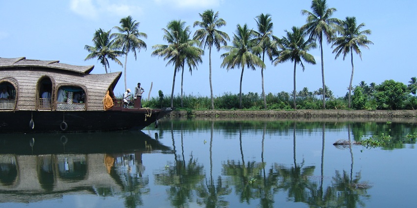A houseboat navigating Vembanad Lake, surrounded by palm trees and shimmering waters.