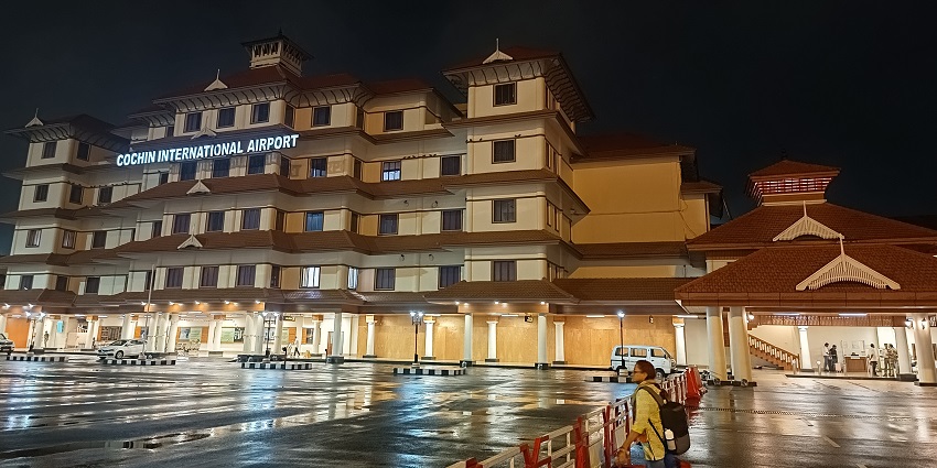 Koch International Airport at night with the lit buildings, parked cars and a woman.