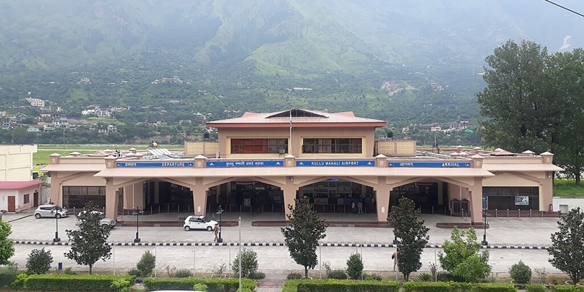 Kullu Manali Airport from the front with a modern building, a signboard, and parked cars.