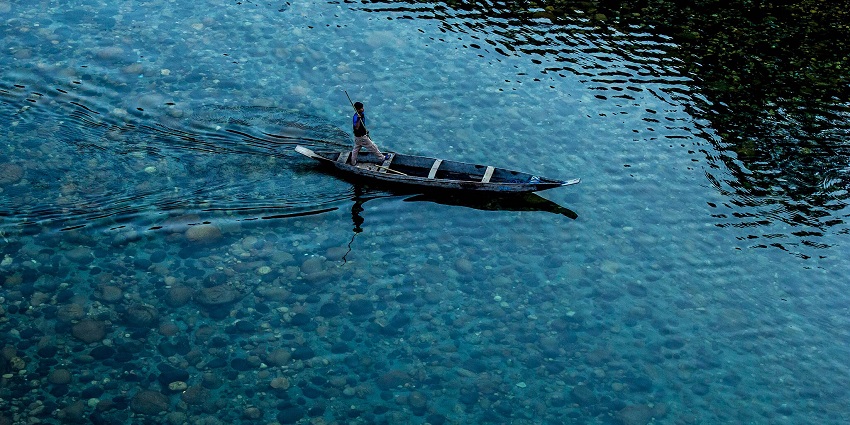 An image of the clear water in the cleanest lake in Meghalaya, surrounded by lush green forests.