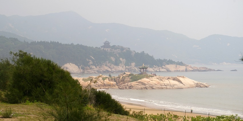 Coastal view of the Hundred Step Beach with a rocky outcrop and misty mountains.