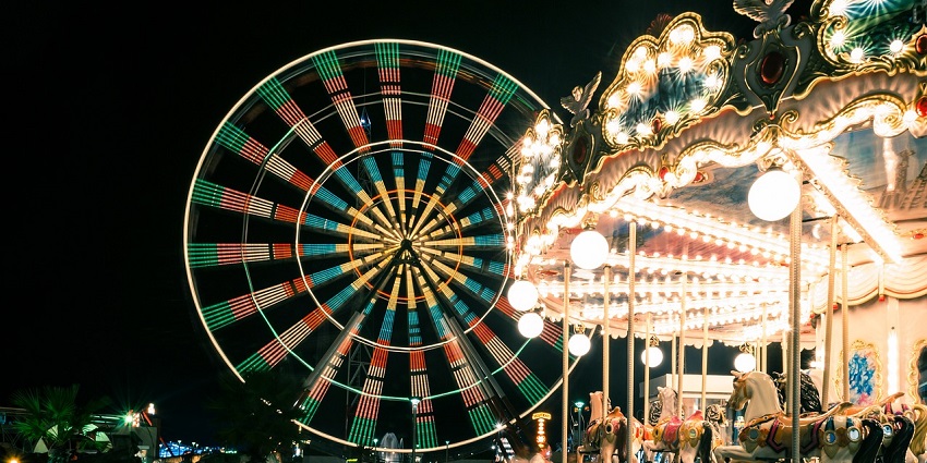 An image of a brightly lit Ferris wheel, carousel and carnival rides at night in an amusement park