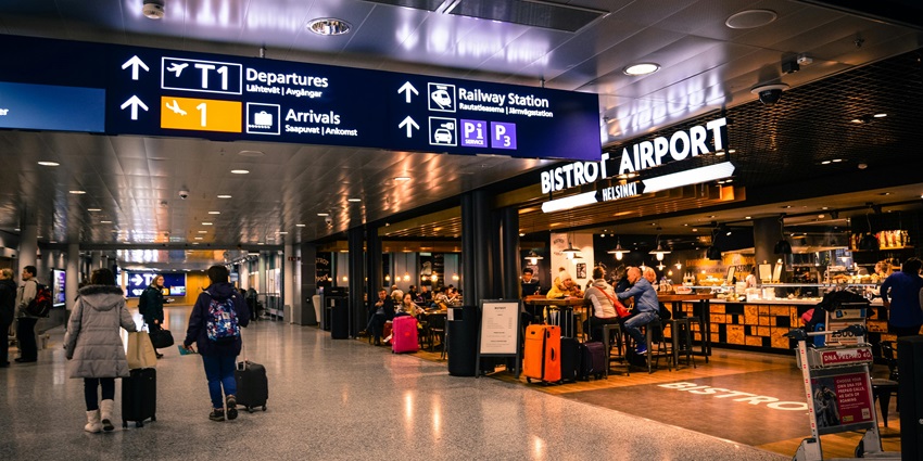 Inside of an airport showing a bistro, signboards, and people sitting and walking