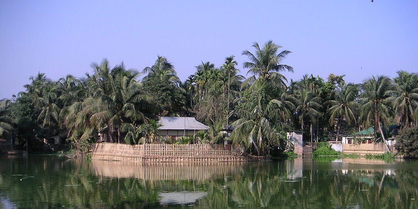 Lake in agartala with a hut-like structure surrounded by palm trees and their reflection