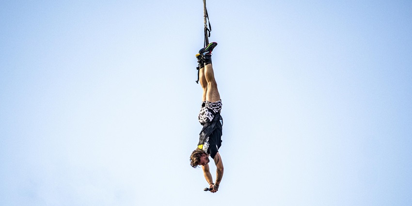 A person bungee jumping, upside down, against blue sky, similar to Bungee in Jagdalpur
