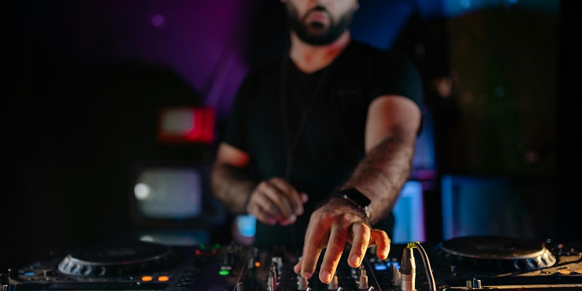 An image of a DJ adjusting controls on a mixer in Jaipur, with colourful lights in the background.