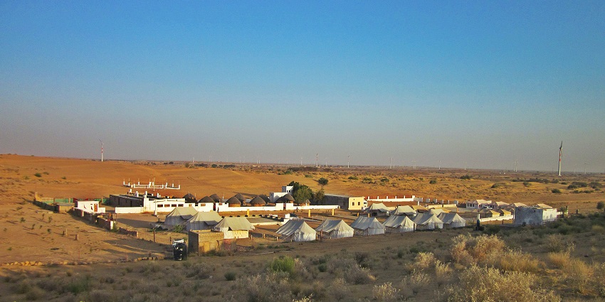 A desert camp with white tents and buildings in an area, view after road trip in India