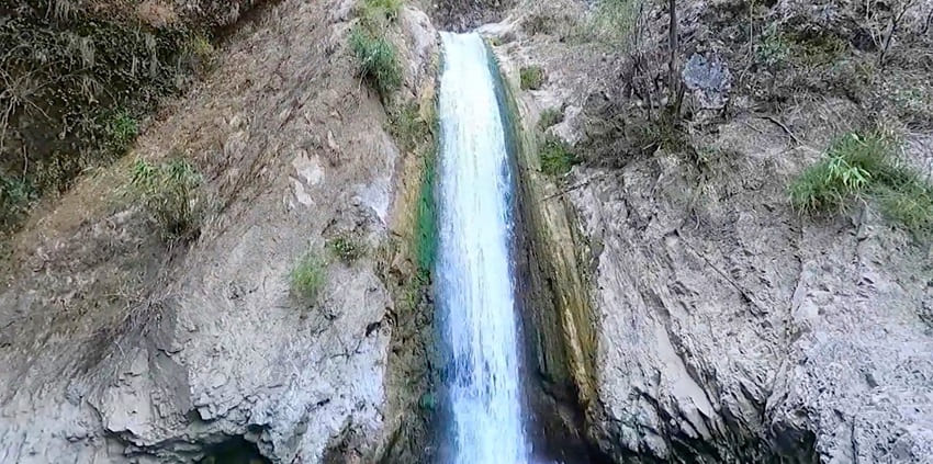 Jharipani Waterfall cascading down rocky cliffs, surrounded by lush greenery and trees