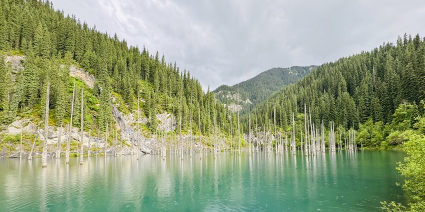 Kaindy Lake with a different-coloured clear waterbody and surrounded by green hills.