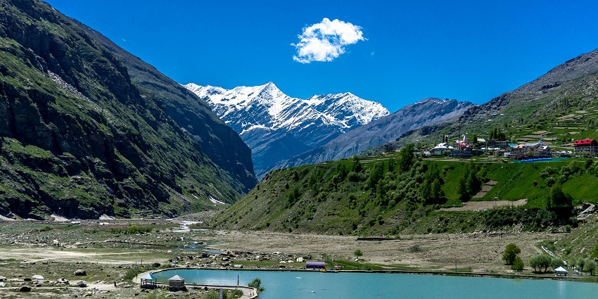 A landscape of a lake with greenery and low snow-covered mountains in the background