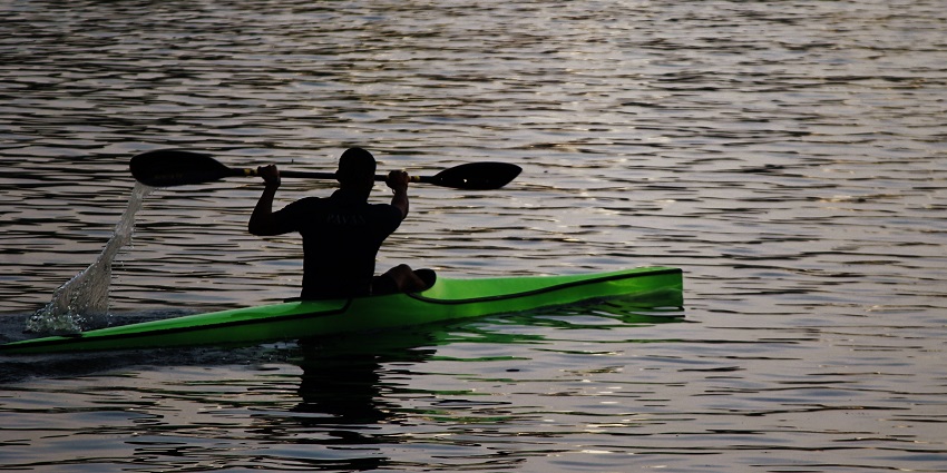 An image of a man rowing his paddle while kayaking in the beautiful waters of Ulsoor Lake.