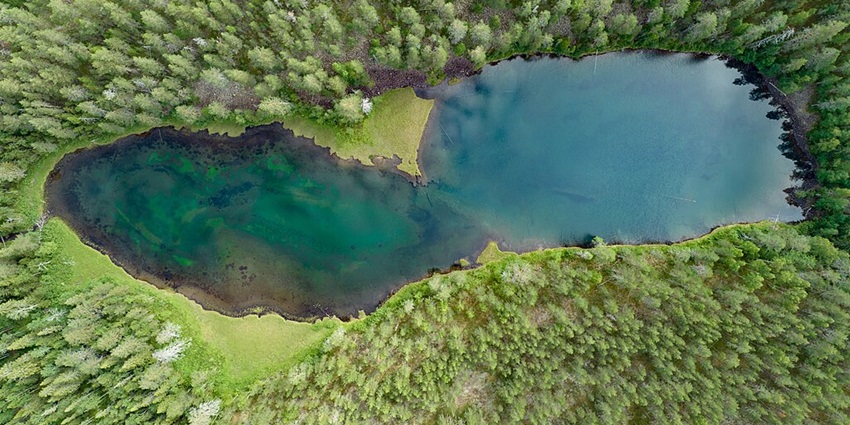 An aerial view of a goggle-shaped lake amid lush greenery in a region