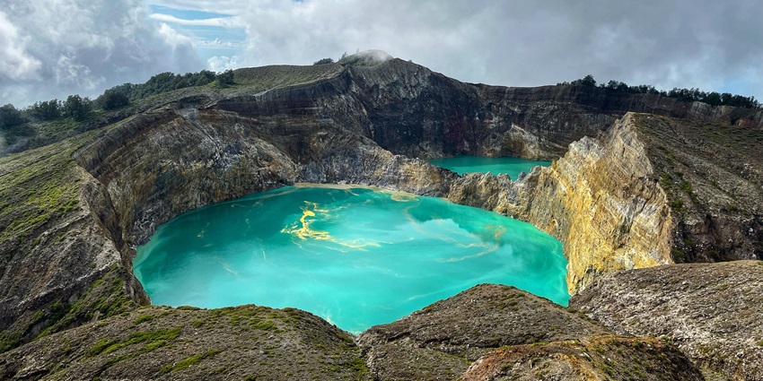 Kelimutu crater lakes with a cyan water body surrounded by stone walls and another lake.