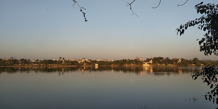 Lake in Indore with a large water body, small tree branches, distant greenery and buildings