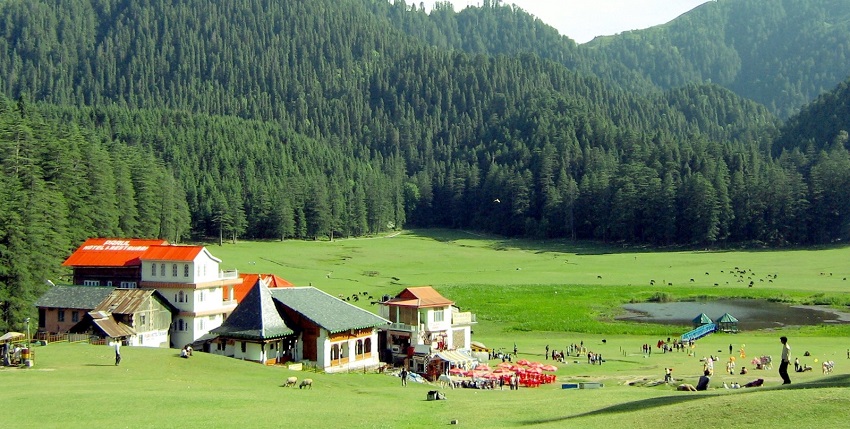 Khajjar Lake with people sitting and standing, small buildings and hills in the background