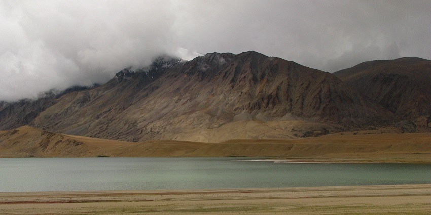 Kiagar tso with a still water body, sandy shorelines and mountains covered in clouds