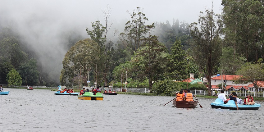 A group of tourists enjoy boating in the Kodaikanal lake with mist in the background