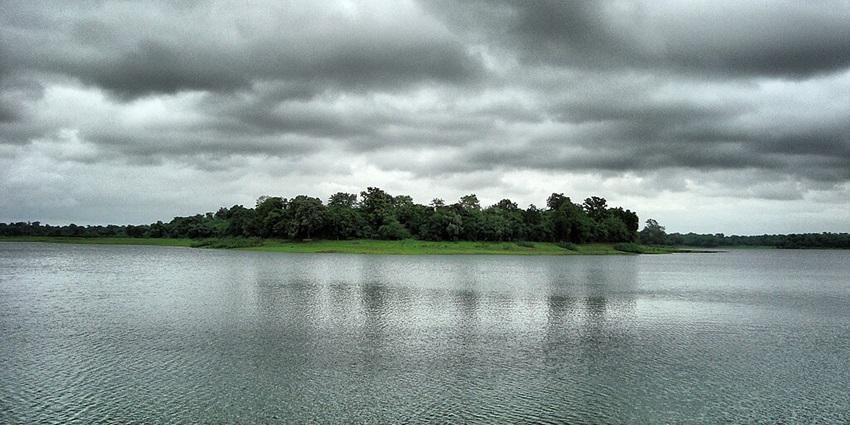 Dam reservoir with a still water body, green shorelines and trees under a cloudy sky