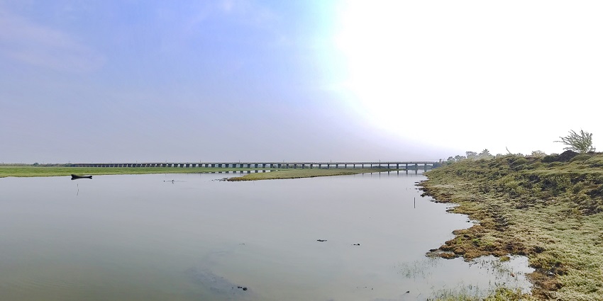 Kolleru Lake with its green shoreline, distant abandoned boats and a bridge over the lake.