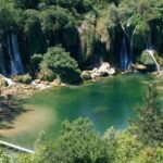 Kravice waterfalls seen from an aerial view surrounded by thick forests with a pool of water in the center.